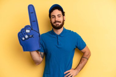 Genç adam mutlu bir şekilde gülümsüyor, eli kalçasında ve kendinden emin. Bir el fan konsepti