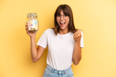 hispanic woman feeling shocked,laughing and celebrating success. candies bottle concept