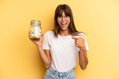 hispanic woman feeling happy and pointing to self with an excited. candies bottle concept