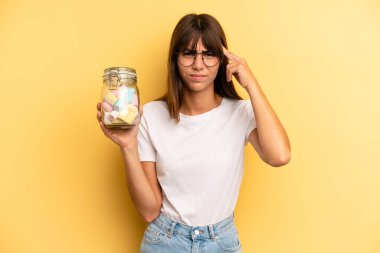 hispanic woman feeling confused and puzzled, showing you are insane. candies bottle concept