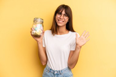 hispanic woman smiling and looking friendly, showing number five. candies bottle concept