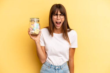 hispanic woman shouting aggressively, looking very angry. candies bottle concept