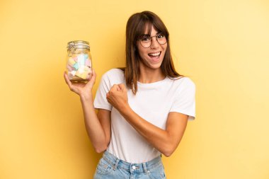hispanic woman feeling happy and facing a challenge or celebrating. candies bottle concept