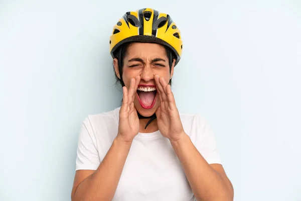 hispanic woman feeling happy,giving a big shout out with hands next to mouth. bike sport concept