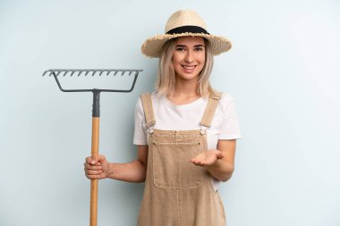 Sarışın kadın mutlu bir şekilde gülümsüyor ve bir konsept sunuyor. Çiftçi ve tırmık kokulu