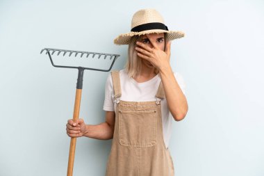 Sarışın kadın şok olmuş, korkmuş ya da korkmuş görünüyor, yüzünü eliyle kapatıyor. Çiftçi ve tırmık kokulu