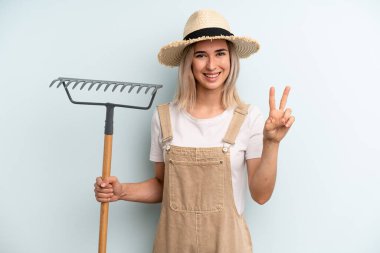 Sarışın kadın gülümsüyor ve arkadaş canlısı görünüyor. İki numarayı gösteriyor. Çiftçi ve tırmık kokulu