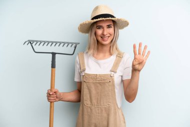 blonde woman smiling and looking friendly, showing number four. farmer and rake cocnept