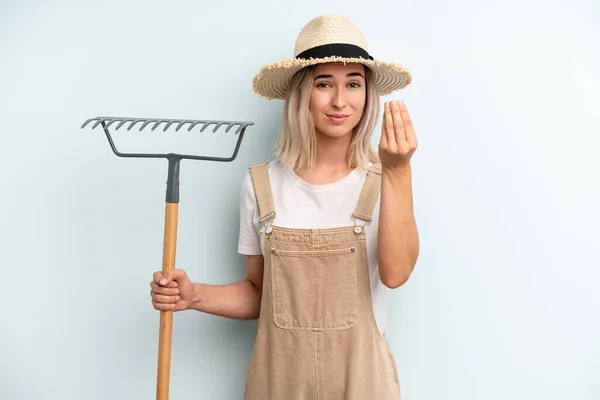 blonde woman making capice or money gesture, telling you to pay. farmer and rake cocnept
