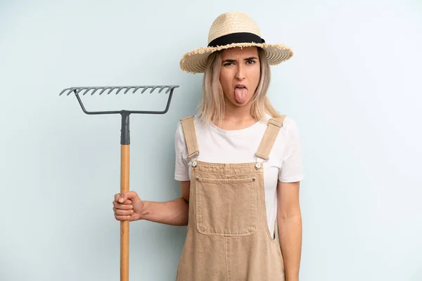 Blonde Woman Feeling Disgusted Irritated Tongue Out Farmer Rake Cocnept — Stockfoto