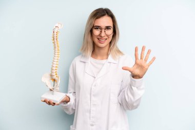 Sarışın kadın gülümsüyor ve arkadaş canlısı görünüyor, beş numarayı gösteriyor. tıp öğrencisi konsepti