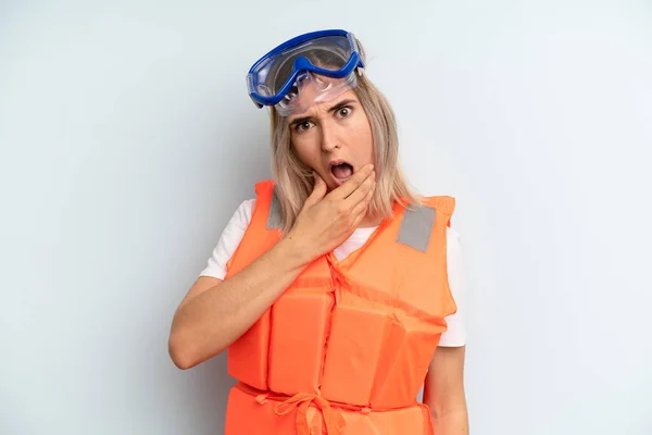 blonde woman with mouth and eyes wide open and hand on chin. life jacket and summer concept