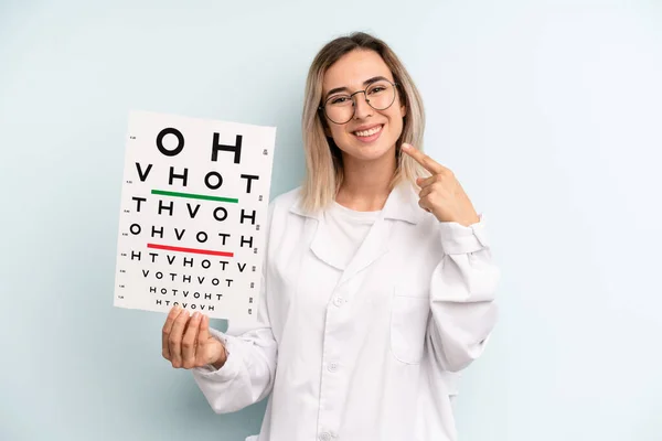 blonde woman smiling confidently pointing to own broad smile. optical vision test concept