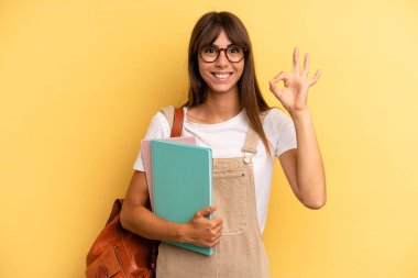 Güzel bir kadın kendini mutlu hissediyor, iyi bir jestle onaylıyor. Üniversite öğrencisi konsepti