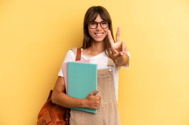 Güzel bir kadın gülümsüyor ve mutlu görünüyor. Zafer ya da barış işareti yapıyor. Üniversite öğrencisi konsepti
