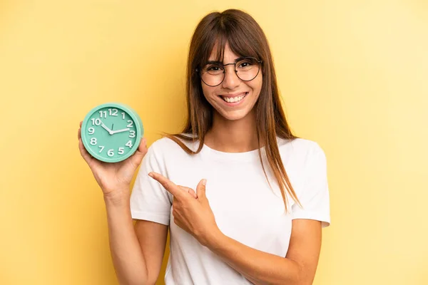 Hispanic Woman Smiling Cheerfully Feeling Happy Pointing Side Alarm Clock — Stockfoto