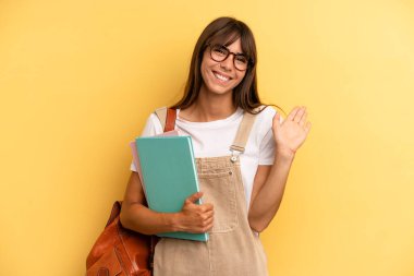 Güzel bir kadın mutlu bir şekilde gülümsüyor, el sallıyor, hoş karşılıyor ve seni selamlıyor. Üniversite öğrencisi konsepti