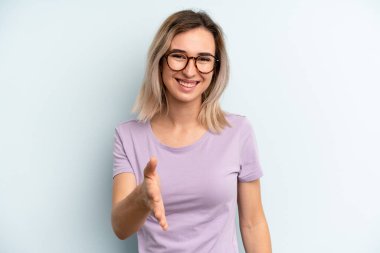 Genç ve güzel bir kadın gülümsüyor, mutlu, kendinden emin ve arkadaş canlısı görünüyor, bir anlaşmaya varmak için tokalaşıyor, işbirliği yapıyor.