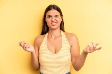 young adult pretty woman shrugging with a dumb, crazy, confused, puzzled expression, feeling annoyed and clueless