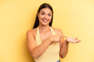 Genç ve güzel bir kadın neşeyle gülümsüyor ve yan taraftaki fotokopi alanını işaret ediyor, bir nesneyi gösteriyor ya da reklamını yapıyor.