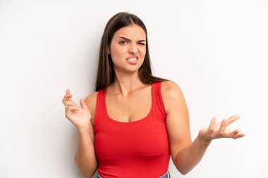 young adult pretty woman shrugging with a dumb, crazy, confused, puzzled expression, feeling annoyed and clueless