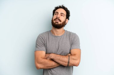 Genç sakallı adam mutlu, gururlu ve umutlu hissediyor, merak ediyor ya da düşünüyor, çapraz kollarla fotokopi çekmeyi bekliyor.