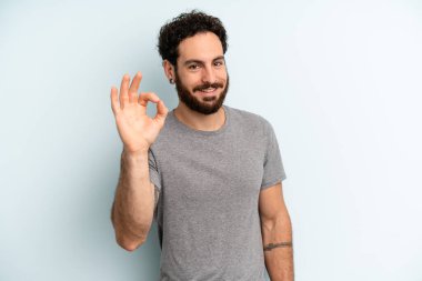 Genç sakallı adam mutlu, rahat ve tatmin olmuş hissediyor. Onayını iyi bir hareketle gösteriyor. Gülümsüyor.