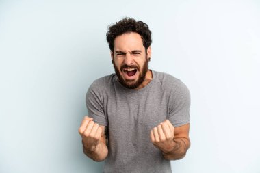 Genç, sakallı bir adam sinirli, sinirli, sinirli ve yumruklarını sıkmış, öfkeli bir şekilde bağırıyor.