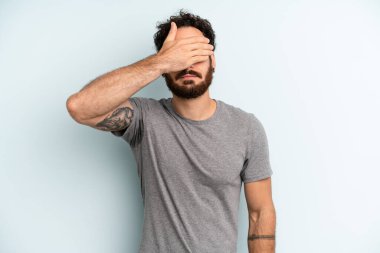 Genç, sakallı bir adam tek eliyle gözlerini kapatıyor korkmuş ya da endişeli hissediyor, merak ediyor ya da körü körüne bir sürpriz bekliyor.