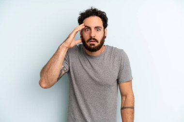 Genç yetişkin sakallı adam mutlu, şaşkın ve şaşırmış görünüyor, gülümsüyor ve inanılmaz ve inanılmaz iyi haberleri fark ediyor.