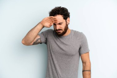 Genç, sakallı, stresli, yorgun ve hayal kırıklığına uğramış, alnından ter damlayan, umutsuz ve bitkin hisseden bir adam.