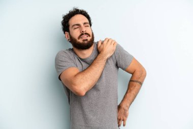 Genç, sakallı bir adam yorgun, stresli, endişeli, hayal kırıklığına uğramış, sırtı ya da boynu ağrıyan