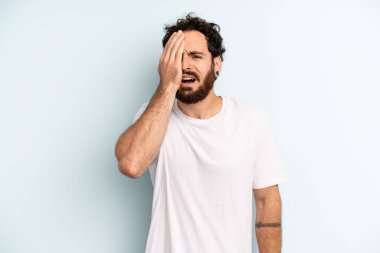 Genç, sakallı bir adam uykulu, sıkılmış ve esniyor, baş ağrısı ve yüzünün yarısını kaplayan bir eliyle