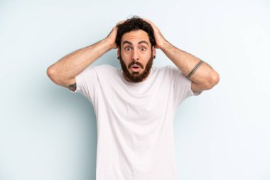 Genç, sakallı, heyecanlı ve şaşırmış görünen, ağzı açık, iki eli başında, kendini şanslı bir kazanan gibi hisseden bir adam.