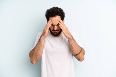 Genç, sakallı bir adam stresli ve hayal kırıklığına uğramış görünüyor. Baskı altında çalışıyor, başı ağrıyor ve sorunları var.