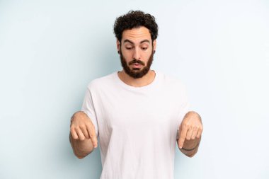 Genç, sakallı, ağzı açık bir adam iki eliyle aşağıya bakıyor, şaşkın, şaşkın ve şaşırmış görünüyor.