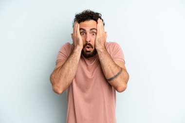 Genç, sakallı, mutsuz, korkmuş ya da endişeli görünen, ağzı açık ve iki kulağını da elleriyle kapatan genç bir adam.