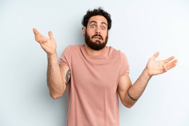 young adult bearded man shrugging with a dumb, crazy, confused, puzzled expression, feeling annoyed and clueless