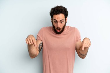 Genç, sakallı bir adam şok olmuş, ağzı açık ve şaşırmış hissediyor. İnançsızlığa ve şaşkınlığa doğru bakıyor ve işaret ediyor.