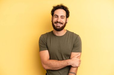 Genç, sakallı bir adam utangaç ve neşeli bir şekilde gülüyor, arkadaş canlısı, olumlu ama güvensiz bir tavırla.