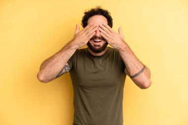 Genç yetişkin sakallı adam gülümsüyor ve mutlu hissediyor, iki eliyle gözlerini kapatıyor ve inanılmaz bir sürpriz bekliyor.