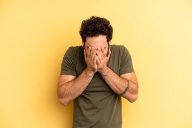 Genç, sakallı bir adam üzgün, hayal kırıklığına uğramış, gergin ve depresif hissediyor. İki eliyle yüzünü kapatıyor, ağlıyor.
