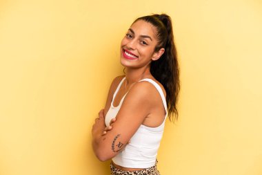 İspanyol asıllı güzel bir kadın kameraya çapraz kollarıyla gülümsüyor ve mutlu, kendinden emin, tatmin olmuş bir yüz ifadesi var.