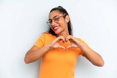 İspanyol güzel kadın gülümsüyor ve mutlu, sevimli, romantik ve aşık, iki eliyle kalbi şekillendiriyor.