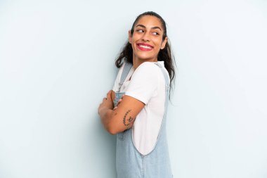 İspanyol güzel kadın neşeyle gülümsüyor, mutlu, tatmin olmuş ve rahatlamış hissediyor, kollarını kavuşturup yan tarafa bakıyor.