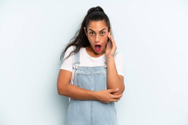 İspanyol güzel kadın şok ve inançsızlık içinde ağzı açık, elleri yanağında ve kolları çaprazlanmış, sersemlemiş ve şaşırmış hissediyor