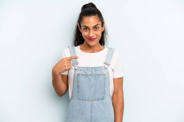 İspanyol güzel kadın gururlu, kendinden emin ve mutlu görünüyor, gülümsüyor ve kendini işaret ediyor ya da bir numara işareti yapıyor.