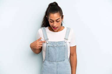 İspanyol güzel kadın neşeyle gülümsüyor, yere bakıyor ve göğsüne işaret ediyor.