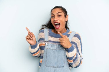 Hispanik güzel kadın neşeli ve şaşırmış hissediyor, şok olmuş bir ifadeyle gülümsüyor ve bir tarafı işaret ediyor.