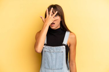 İspanyol görünümlü güzel bir kadın şok olmuş, korkmuş ya da korkmuş görünüyor. Yüzü elle kaplanmış ve parmaklarının arasından gizlice bakıyor.